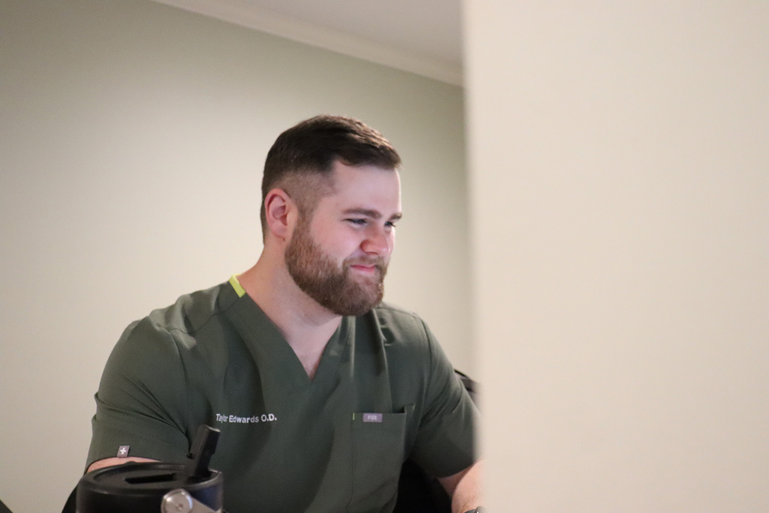 Dr. Taylor Edwards at Work – Magnolia Eye Group Dr. Taylor Edwards, wearing green scrubs, focuses on a computer screen while working at Magnolia Eye Group. – Magnolia Eye Group