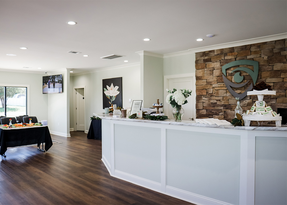 Welcoming Office Interior – Magnolia Eye Group A clean, modern reception area with wood floors, floral decor, and an eye-themed logo on a stone accent wall – Magnolia Eye Group.