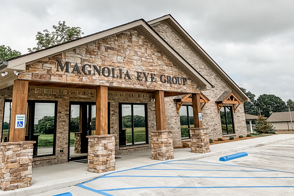 Front View of Magnolia Eye Group – Magnolia Eye Group A stone and wood-accented eye clinic with large windows and accessible parking spaces in front – Magnolia Eye Group.