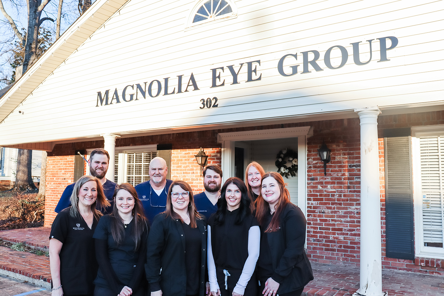 Meet the Team at Magnolia Eye Group – Magnolia Eye Group Dr. Steve Edwards, Dr. Hunter Edwards, Dr. Taylor Edwards, Sarah Thrower, and staff smile together outside the Magnolia Eye Group building. – Magnolia Eye Group