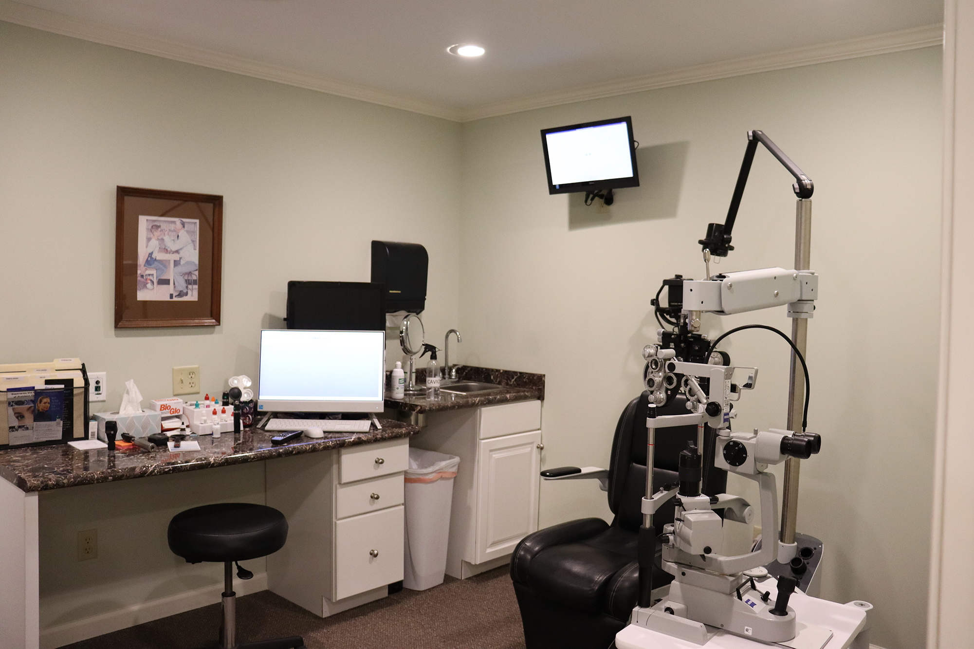 An exam room with an eye exam chair, diagnostic equipment, a computer workstation, and a countertop with medical supplies – Magnolia Eye Care.