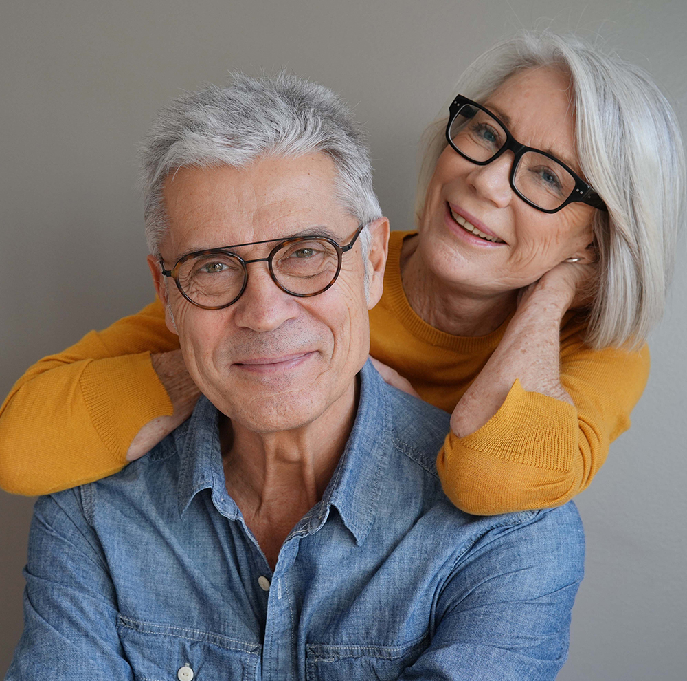 Clear Vision and Lasting Smiles – Magnolia Eye Group An older couple wearing stylish glasses smiles warmly while embracing each other. – Magnolia Eye Group